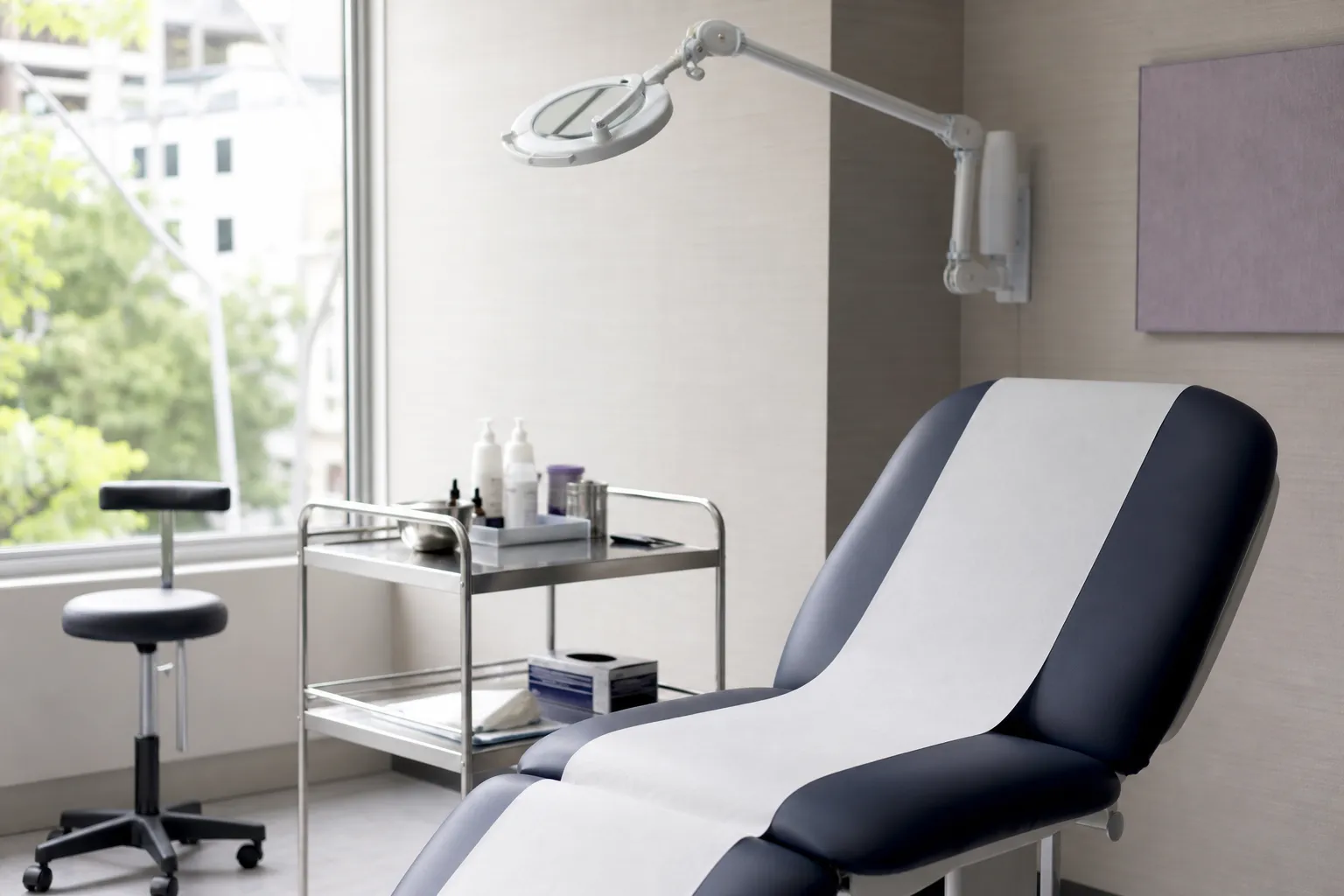 Salle de soin vide et claire : fauteuil garni de papier propre, chariot en inox, lampe articulée éteinte